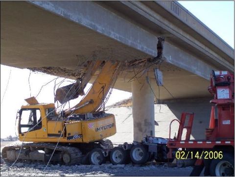 1995 Ford Bronco - A Hyundai excavator is actively demolishing a damaged concrete bridge structure, with a red trailer visible on the right side of the scene.