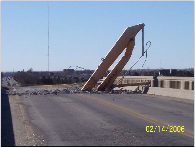 Yellow Hyundai demolition equipment on a damaged bridge, debris scattered on the road