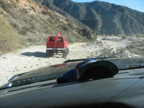 1987 Ford Bronco - A red Ford Bronco is driving on a dirt road in a mountainous area. A Confederate flag is attached to the back of the vehicle.
