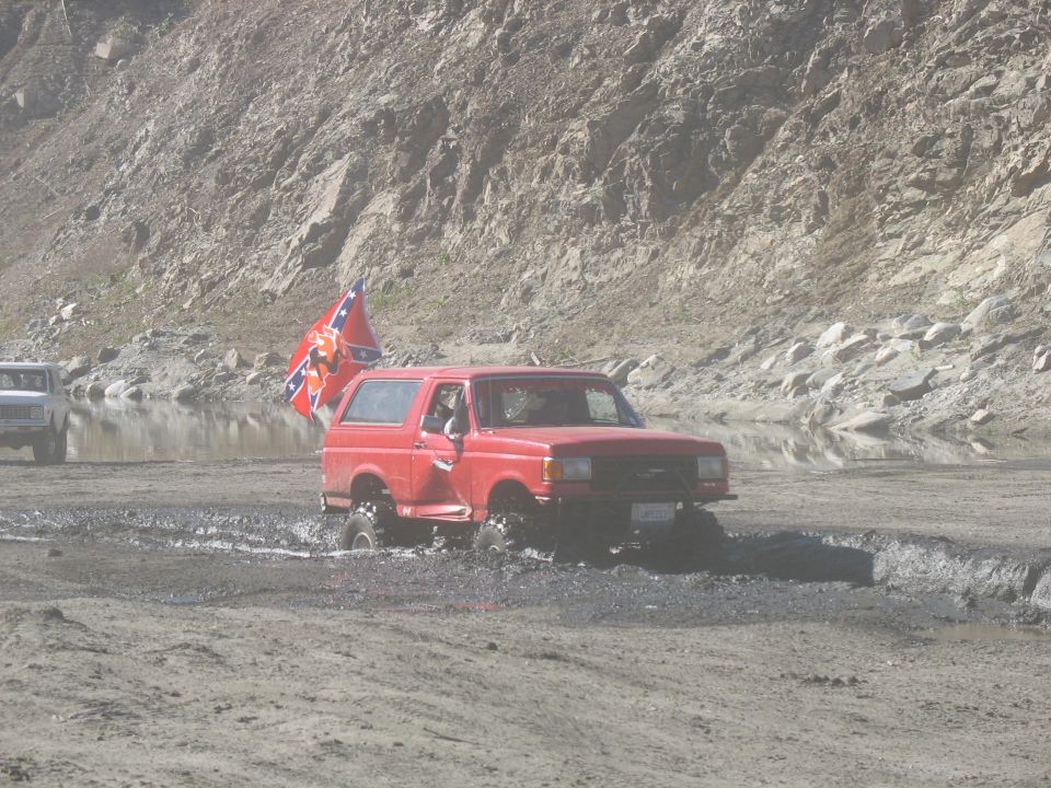 Red Ford Bronco driving through mud with Confederate flag.