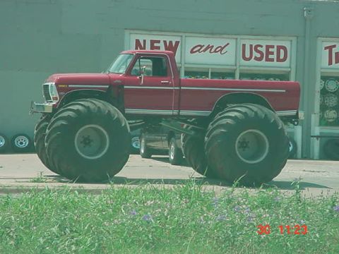 1989 Ford Bronco - This modified pickup truck features massive tires, transforming it into a monster truck. The vehicle is seen parked in front of a business…