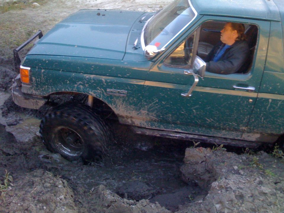 Green Ford Bronco stuck in mud, driver visible.