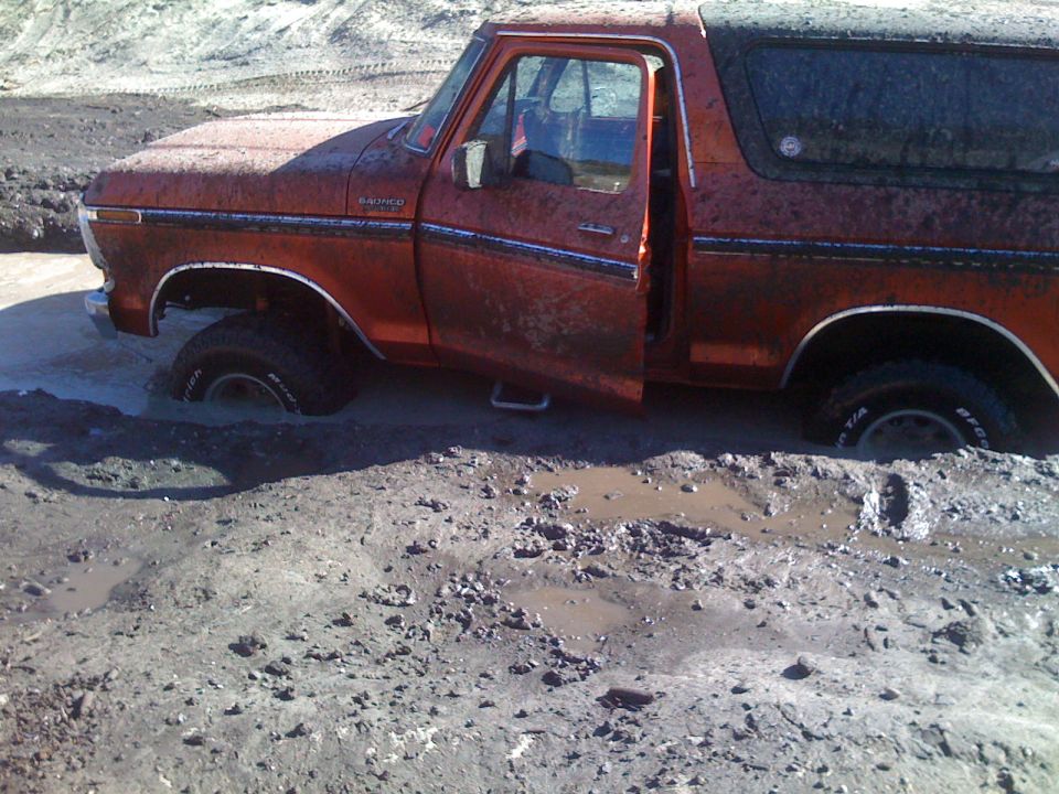 Orange Ford Bronco stuck in mud, driver's side door open.