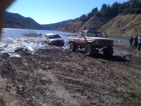 1979 Ford Bronco - Two off-road vehicles are stuck in mud near a body of water. A lifted pickup truck is in the foreground, while a white SUV is partially sub…