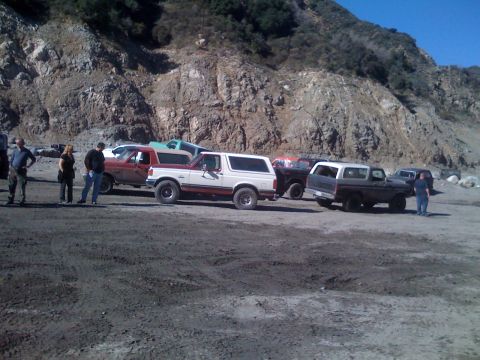 1979 Ford Bronco - Several Ford Bronco SUVs are parked on a dirt lot with a rocky hillside in the background. One red and white Bronco is in the foreground, w…