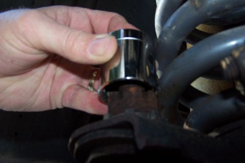 1990 Ford Bronco - A hand is holding a chrome socket over a rusty bolt on what appears to be part of a vehicle's suspension system. The socket is being positi…