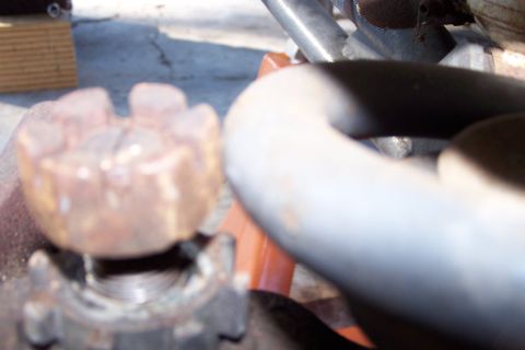 1990 Ford Bronco - A close-up, out-of-focus shot shows a rusty, star-shaped nut on a threaded bolt. A thick, curved metal pipe is visible in the foreground.