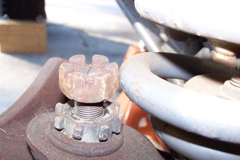 1990 Ford Bronco - A close-up shot shows a rusted castle nut and washer assembly on a threaded bolt, with a portion of a gray coil spring visible to the right.