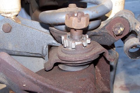 1990 Ford Bronco - A close-up view of heavily rusted suspension components on a vehicle, including a ball joint secured by a castle nut and cotter pin, and a…