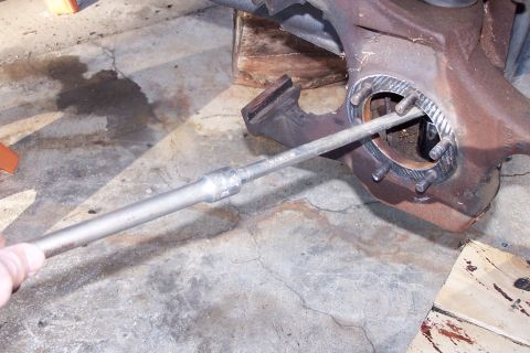 1990 Ford Bronco - A close-up view shows a metal tool inserted into a rusty, bolted metal component, likely part of a vehicle's suspension or drivetrain, rest…