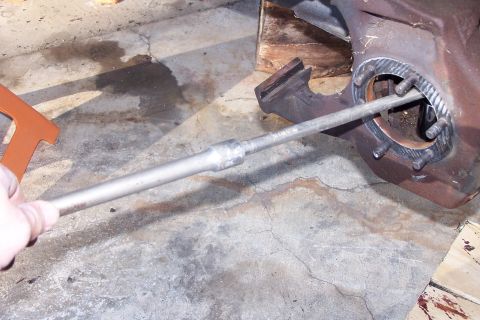 1990 Ford Bronco - A hand holds a metal rod inserted into a rusty metal housing with several bolts around the opening. The scene appears to be a concrete floo…