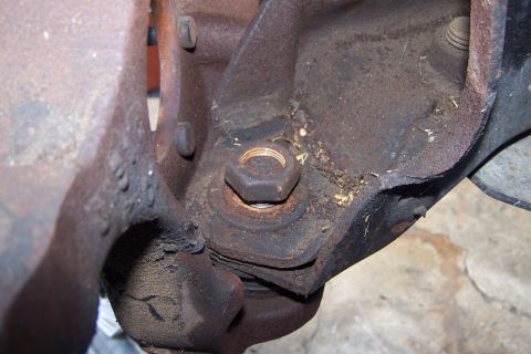 1990 Ford Bronco - This is a close-up view of heavily rusted automotive suspension components, featuring a large hex nut and bolt securing two metal brackets.…
