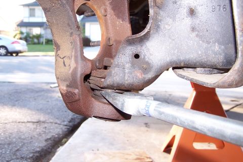 1990 Ford Bronco - A close-up view shows a mechanic using a pry bar to separate a rusty suspension component from a vehicle frame. The vehicle is supported by…