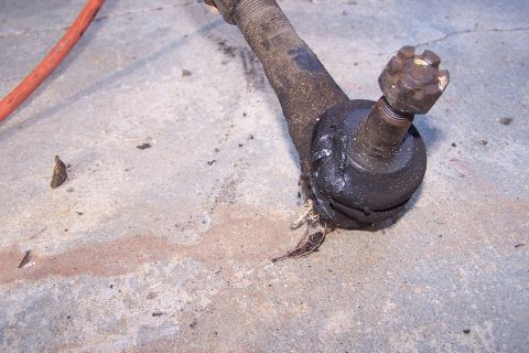 1990 Ford Bronco - A close-up view of a worn and greasy tie rod end with a castle nut. The part is resting on a concrete surface next to a red hose.