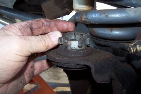 1990 Ford Bronco - A mechanic's greasy hand is shown adjusting a castle nut on a suspension component, likely a ball joint, on a vehicle. The vehicle appears…
