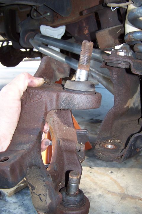 1990 Ford Bronco - A person's hand is holding a rusty suspension part, likely from a 1990 Ford Bronco. The part appears to be a steering knuckle with a ball j…