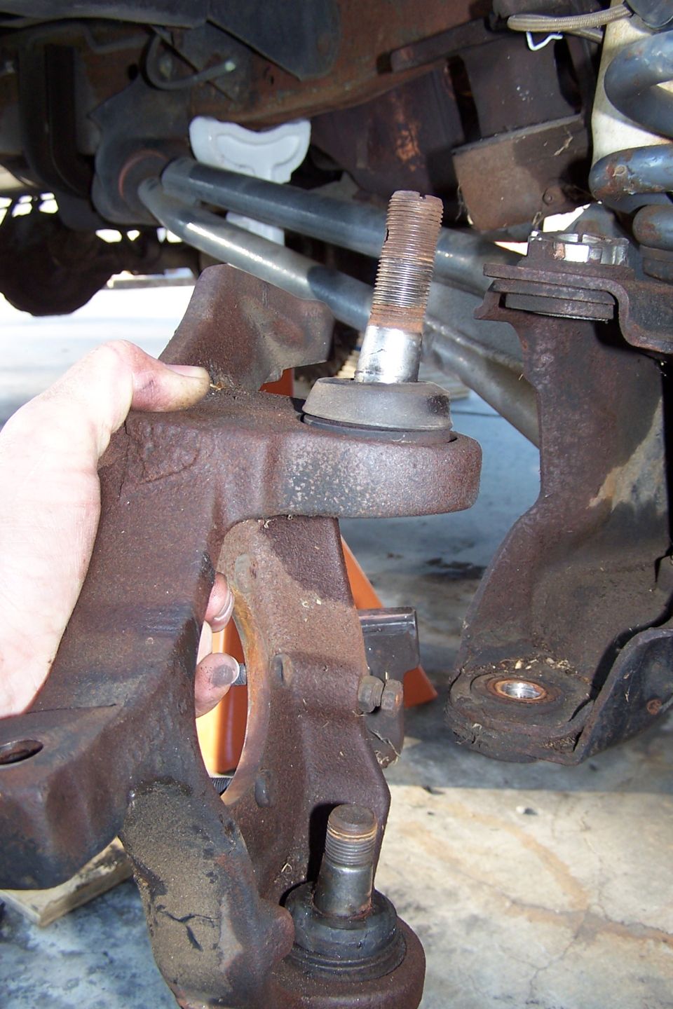 Rusty suspension part with ball joint being held by a hand.