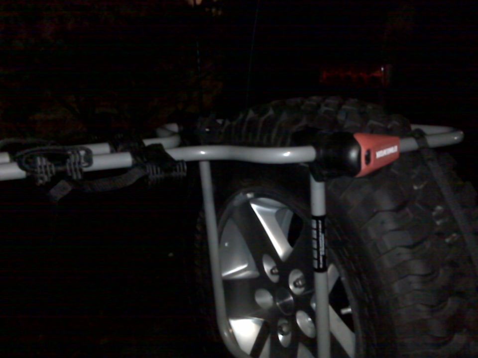 Spare-tire-mount bike rack strapped to a rear-mounted mud-terrain spare at night