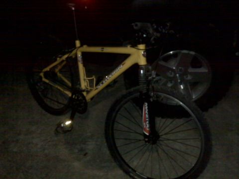 2008 Jeep Wrangler - A yellow mountain bike is parked next to a Jeep Wrangler wheel. The bike has a front suspension fork and a black chainring.