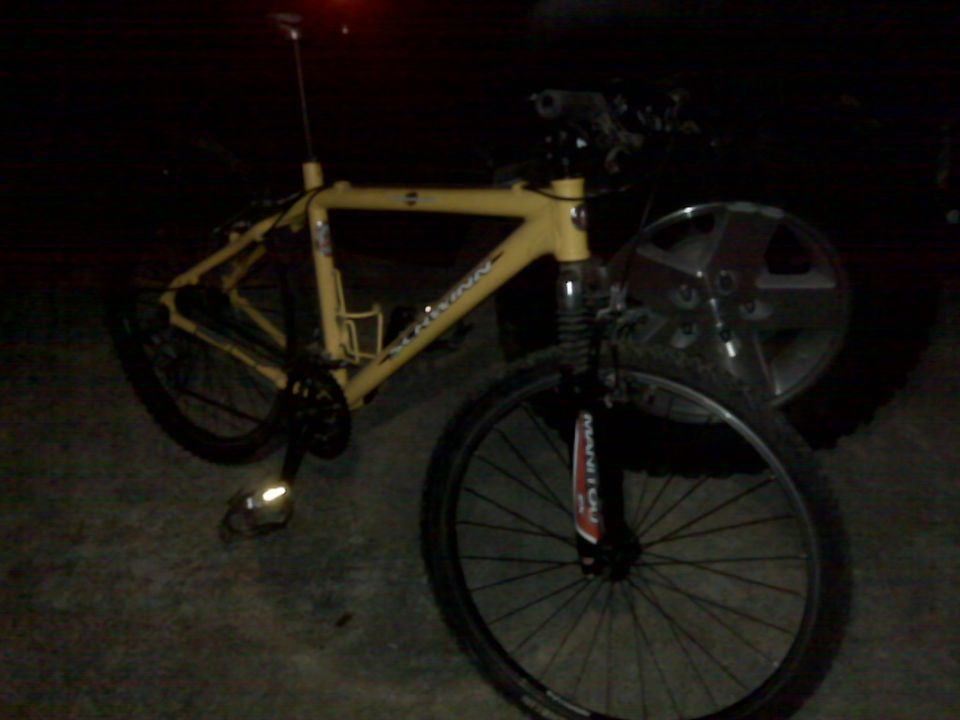 Yellow mountain bike next to a Jeep Wrangler wheel at night.