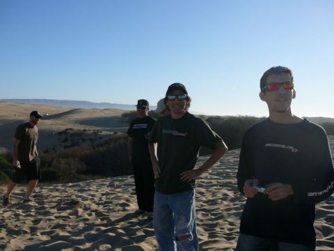1988 Ford Bronco - Four men stand on a sand dune under a clear blue sky. The man in the foreground on the right wears a dark long-sleeved shirt and sunglasses.