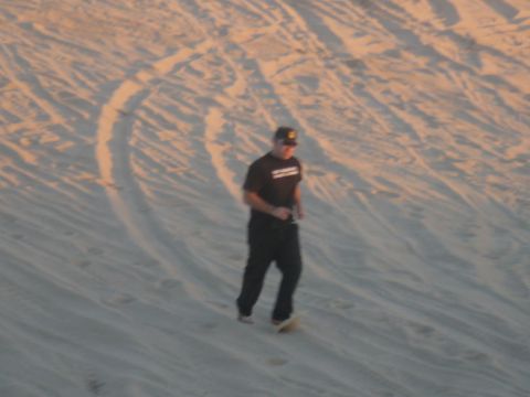 1988 Ford Bronco - A person in a black t-shirt and black pants is walking on a sandy dune, possibly sandboarding.