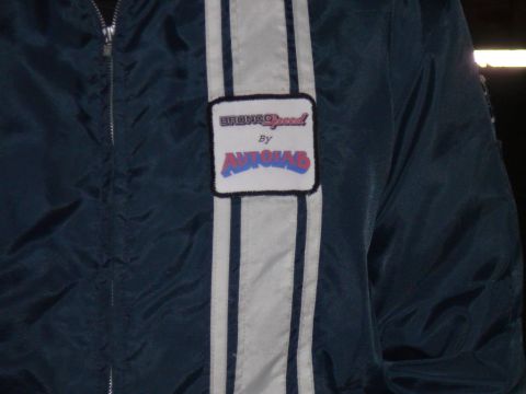 1988 Ford Bronco - A close-up shot of a dark teal jacket with a white stripe down the front, featuring a patch with the text "BRONCO Speed By AUTOSAB".