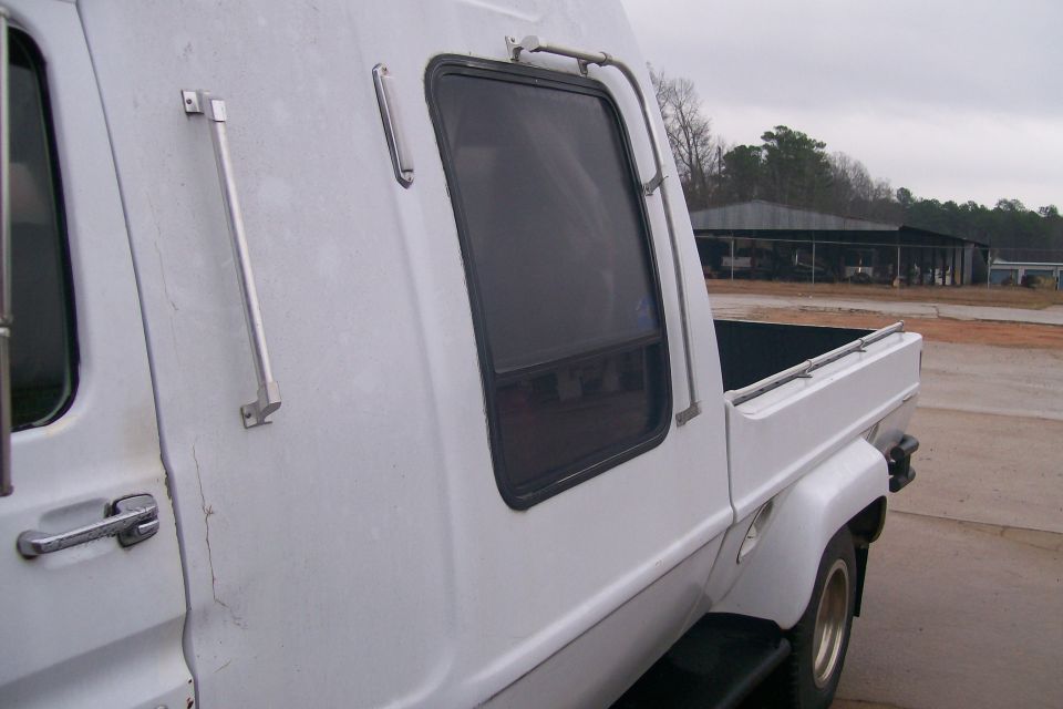 Side view of a white custom truck camper with a dark window and chrome door handle.