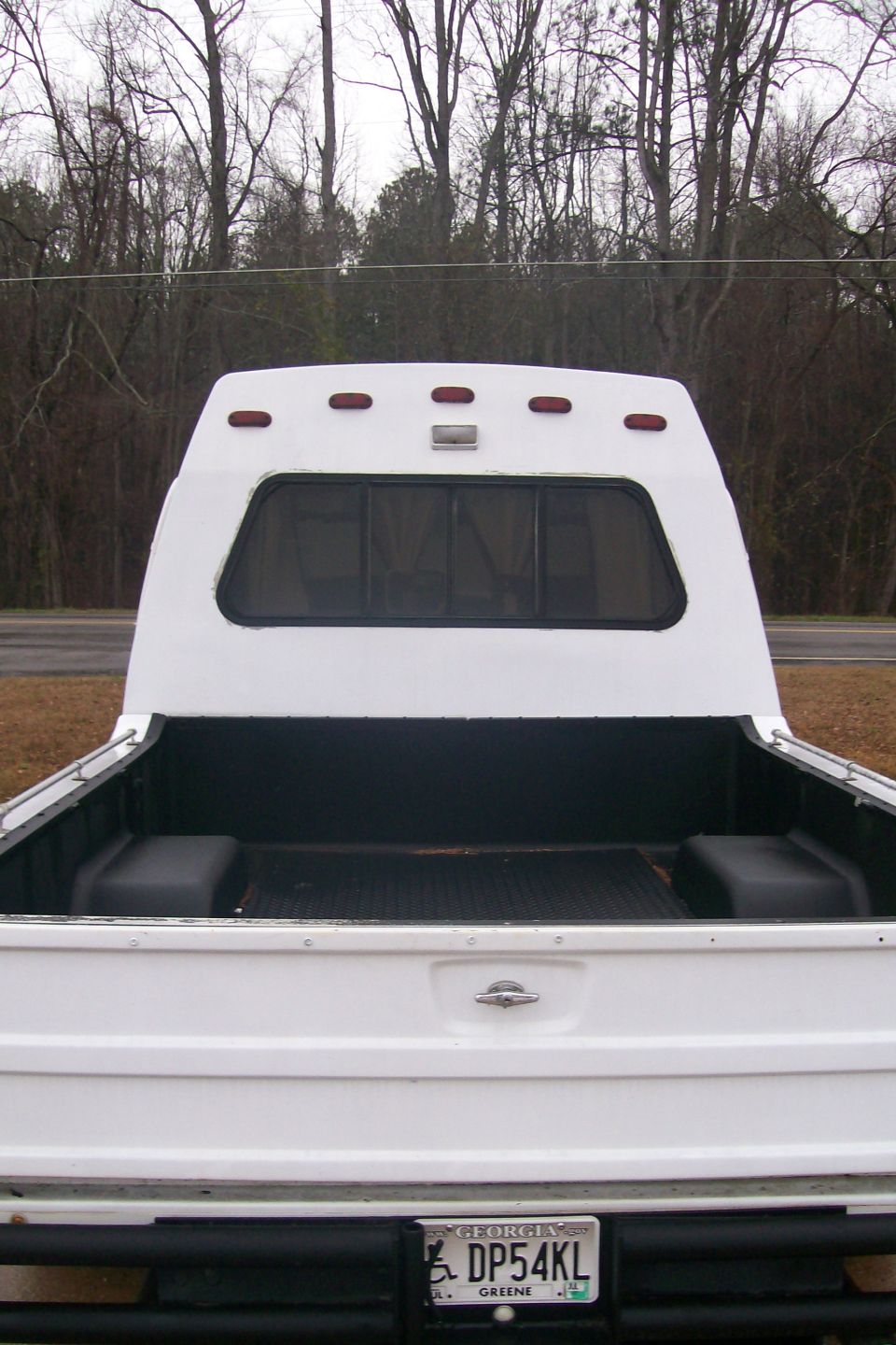 Rear view of a white pickup truck with a white camper shell and Georgia license plate.