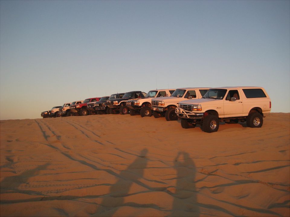 A line of modified Ford Broncos parked on a sand dune.