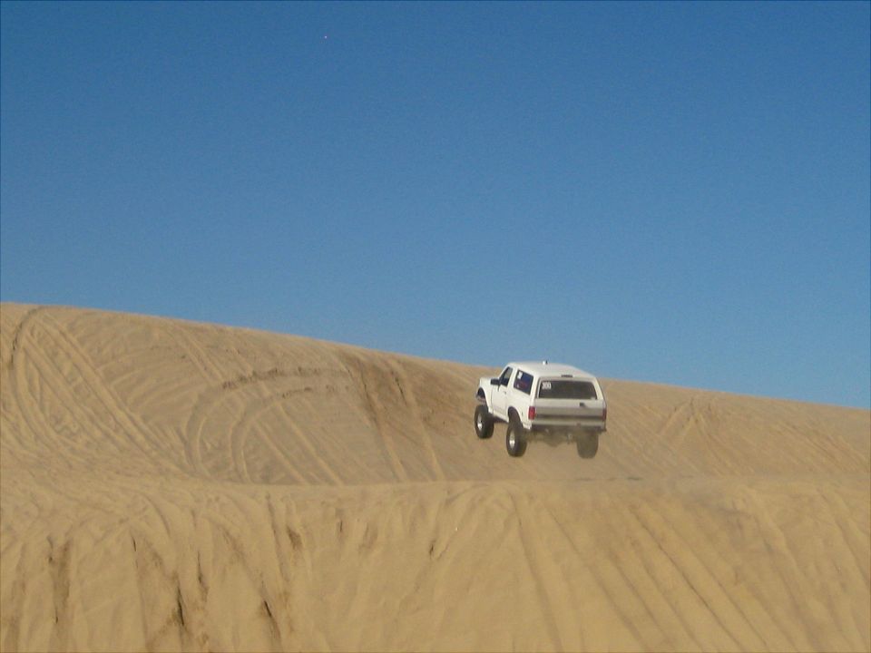 White 1996 Ford Bronco jumping over a sand dune.