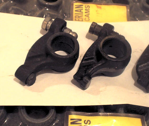 Two black metal rocker arms with bolts and nuts, on a white surface with a yellow "ERIAN CAMS" label.