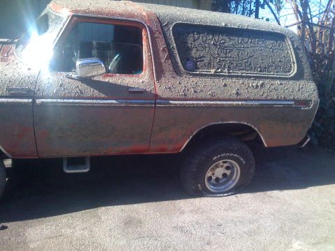 1979 Ford Bronco - A heavily mud-covered vintage Ford Bronco is parked on a paved surface. Text is written in the dirt on the rear window, reading "DO NOT QUE…