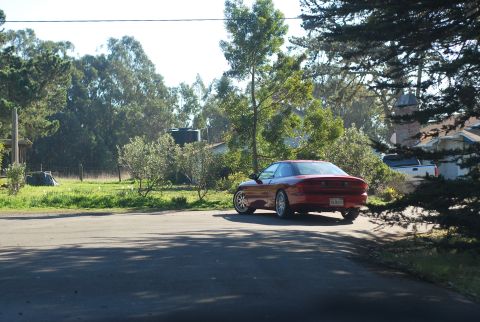 1994 Ford Probe - A red 1994 Ford Probe is parked on the side of a paved road, with a rural landscape of trees and grass in the background. The car is viewed…