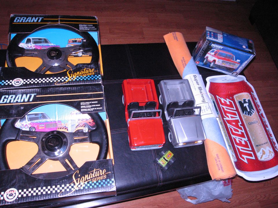 Two Grant steering wheels in boxes, toy trucks, and a Tecate beer can on a black surface.