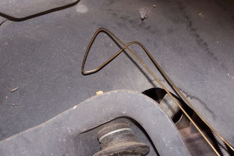 1990 Ford Bronco - A close-up view shows a bent metal brake line or fuel line resting on the underside of a vehicle. A portion of the suspension and frame are…