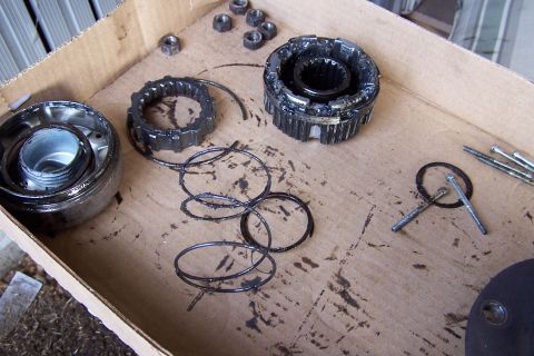1990 Ford Bronco - A collection of used automotive parts, including gears, nuts, and bolts, are laid out on a dirty cardboard surface. The parts appear to be…