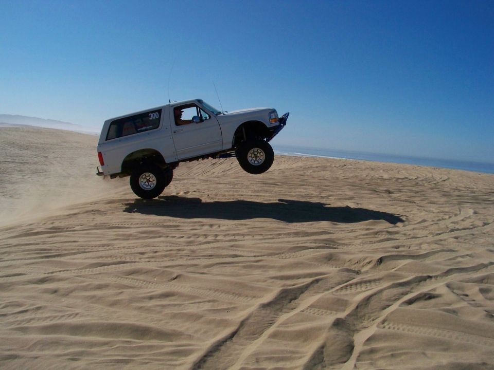 White Ford Bronco jumping over a sand dune.
