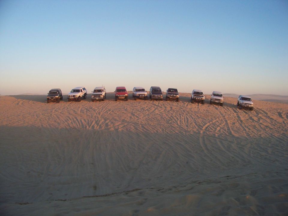Multiple SUVs parked in a line on a sand dune.