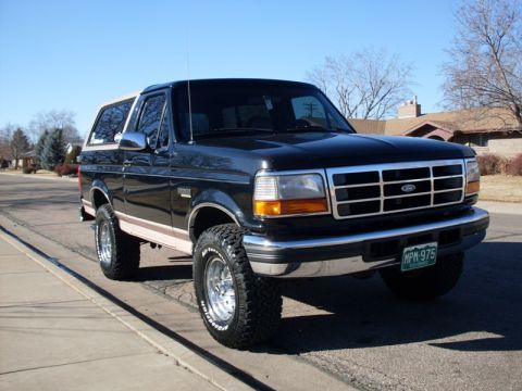1996 Ford Bronco - A lifted black 1996 Ford Bronco with a tan top is parked on the side of a residential street. The vehicle has chrome wheels and BFGoodrich…