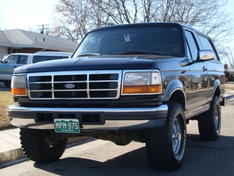 1996 Ford Bronco - A front 3/4 view of a black Ford Bronco parked on a residential street. The vehicle has a chrome grille, aftermarket wheels, and a Colorado…