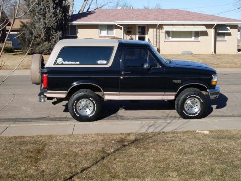 1996 Ford Bronco - A black 1996 Ford Bronco with a tan top is parked on the side of a residential street. The vehicle has a spare tire mounted on the rear and…