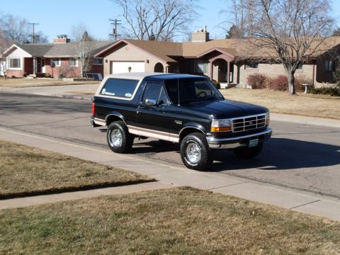1996 Ford Bronco - A black 1990s Ford Bronco with a tan removable top is parked on the side of a residential street. The vehicle is shown from a three-quarter…