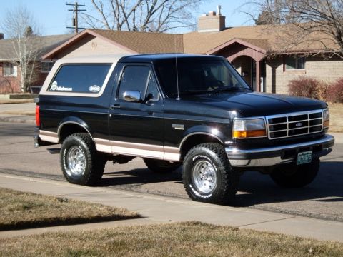 1996 Ford Bronco - A black 1996 Ford Bronco is parked on the side of a residential street. The SUV has a tan top and a brown stripe along the lower body.