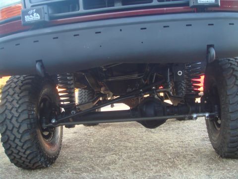 1992 Ford Bronco - The underside of a lifted 1992 Ford Bronco is shown, with a focus on the front suspension and steering components. Large off-road tires and…