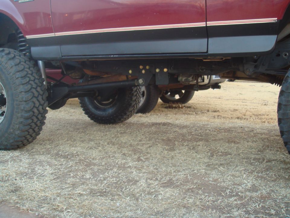 Lifted maroon Ford Bronco undercarriage with large tires and suspension mods.