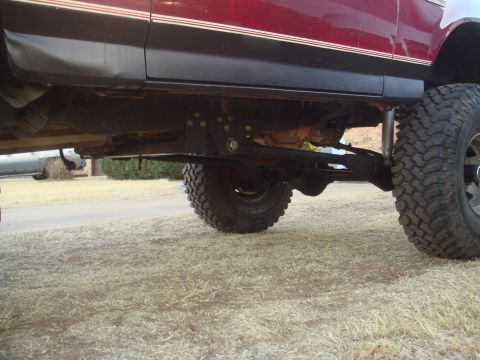 1992 Ford Bronco - A low-angle side view of the undercarriage of a lifted, red SUV, showing the suspension components, exhaust system, and large off-road tire…