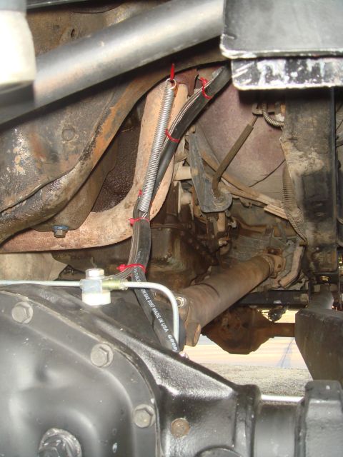 1992 Ford Bronco - A close-up view of the undercarriage of a vehicle, showing the drive shaft, differential housing, and brake lines. A spring is used to supp…