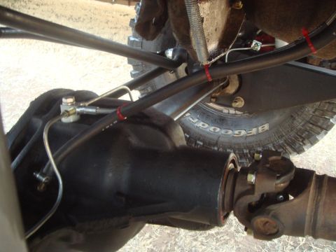 1992 Ford Bronco - A close-up view of the rear differential and driveshaft of a vehicle, with visible suspension components and brake lines. The tire in the b…