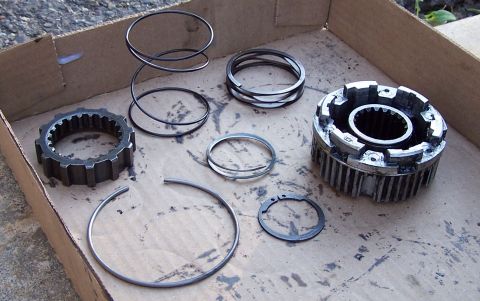 1990 Ford Bronco - A collection of transmission or transfer case parts are laid out on a piece of cardboard. Visible parts include a gear, several rings, a sp…
